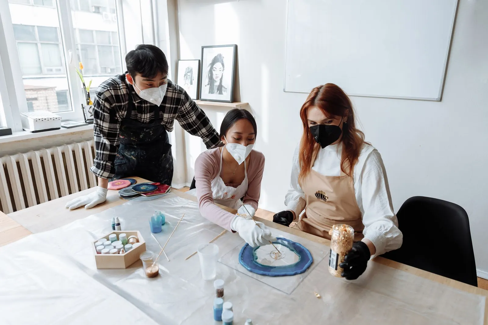 Artists working together using epoxy resin in a creative studio setting with face masks and protective gear. Stock photo illustrating Epigral's expansion story.