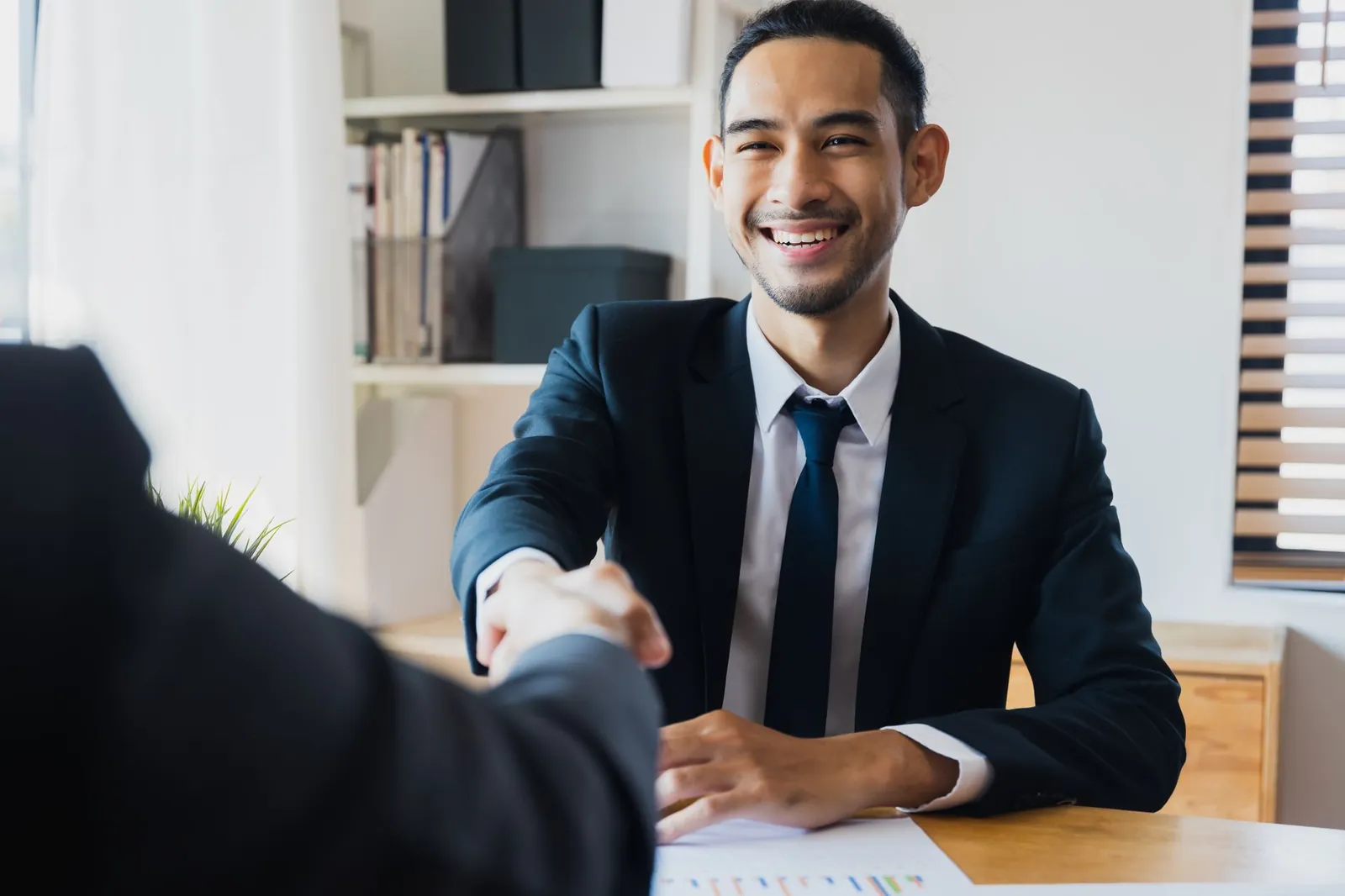 Confident businessman in suit shaking hands at office desk, symbolizing successful partnership. Stock photo illustrating Emerald Finance's fund raise story.