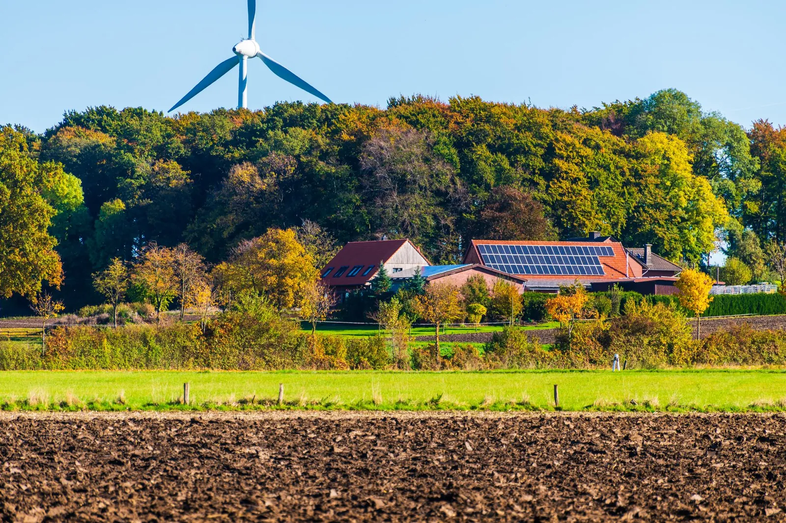 A picturesque sustainable farm featuring wind turbine and solar panels surrounded by vibrant autumn foliage. Stock photo illustrating ACME Solar Holdings' new order story.