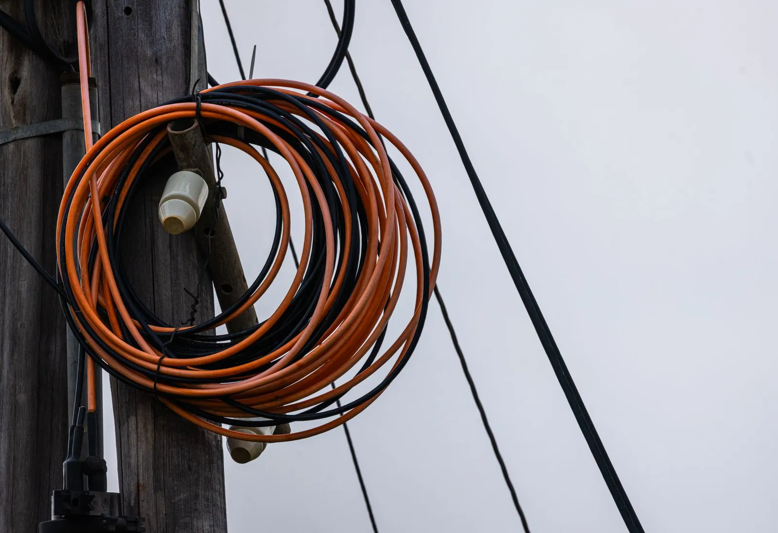 Close-up photo of coiled orange and black electrical wires on a wooden utility pole against a gray sky. Stock photo illustrating Apar Industries' fund raise story.
