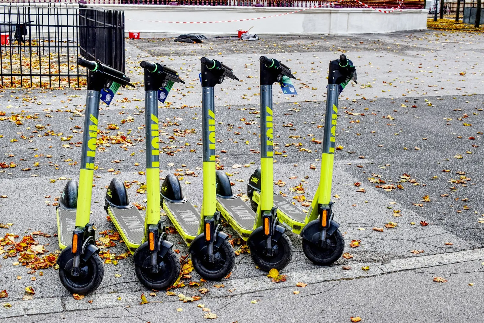 Five lime green e-scooters parked in a row on a leaf-strewn street during autumn. Stock photo illustrating TVS Motor Company's product launched story.
