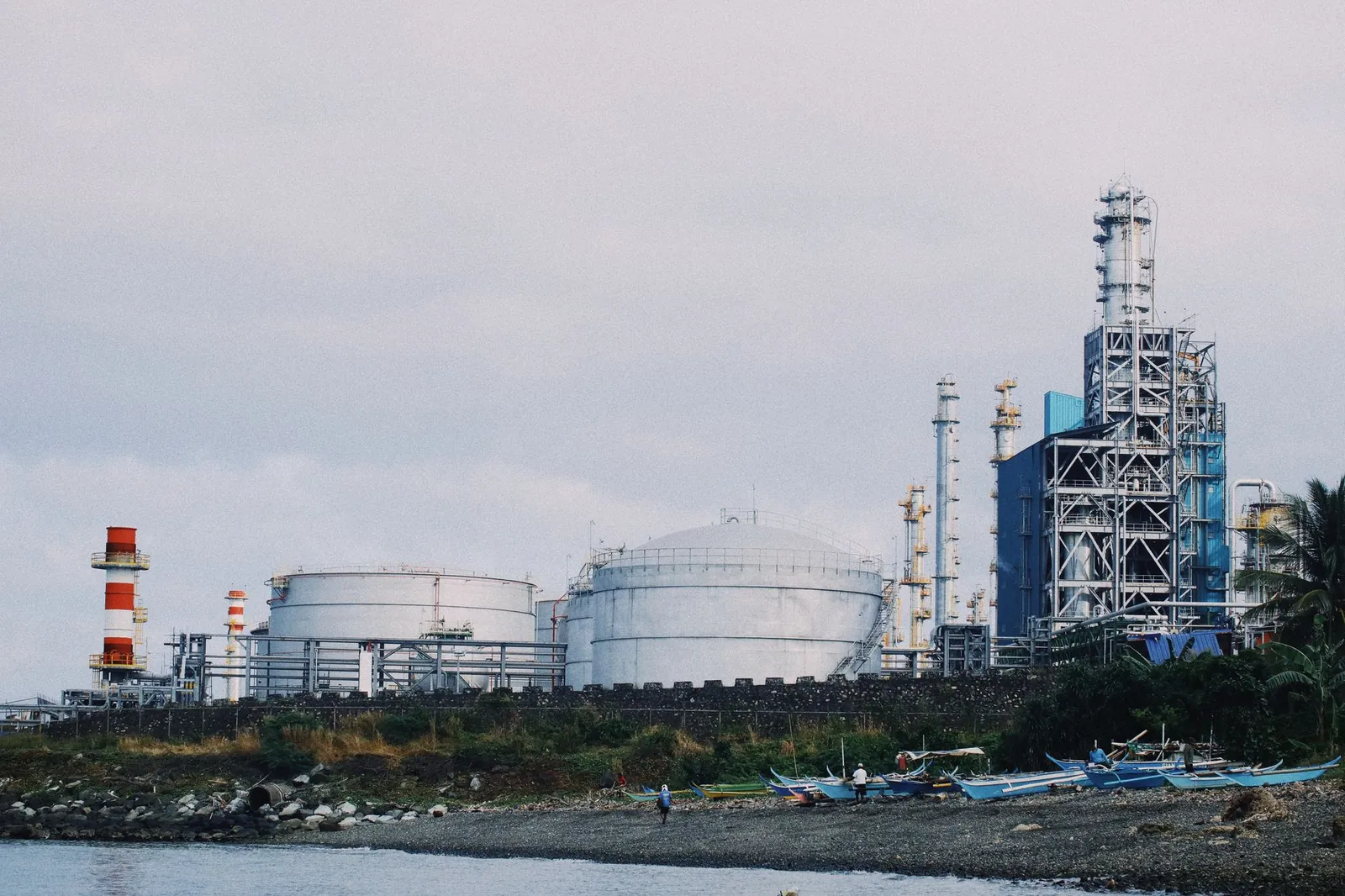 A coastal industrial petrochemical plant with storage tanks and factory structures against a cloudy sky. Stock photo illustrating Praj Industries' partnership story.