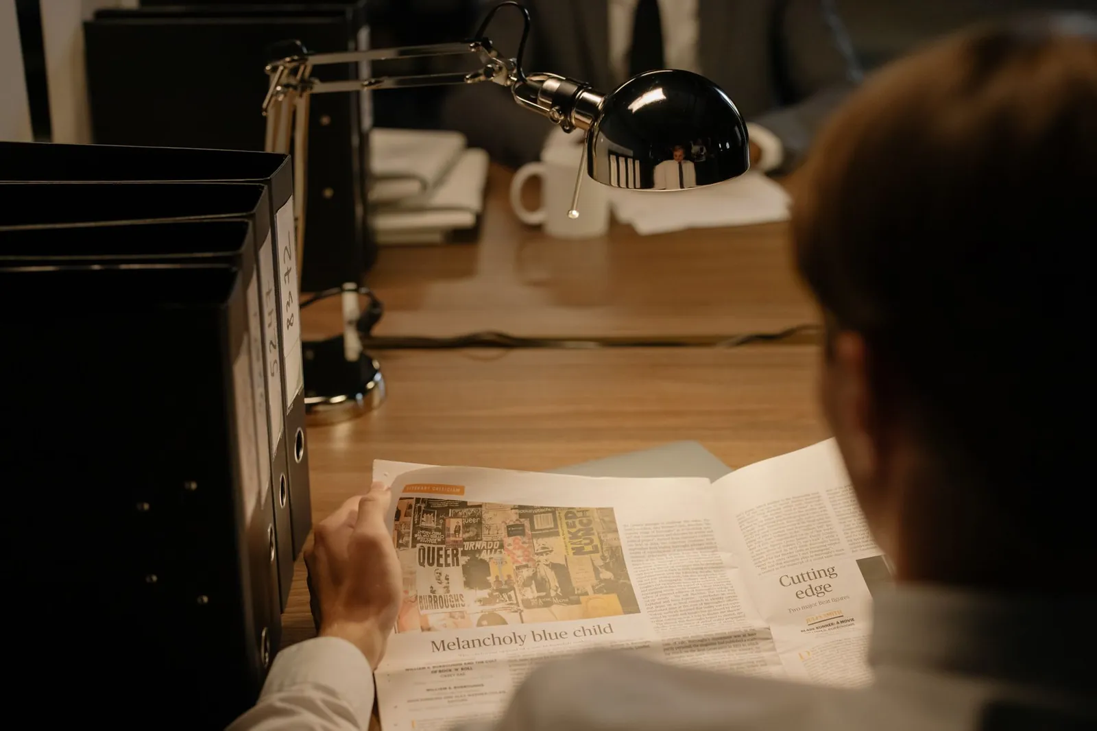 A person reads a newspaper at a desk with a lamp, suggesting investigation work. Stock photo for the ALFA News guide: Understanding Newspaper Publication Filing for Indian Stocks.