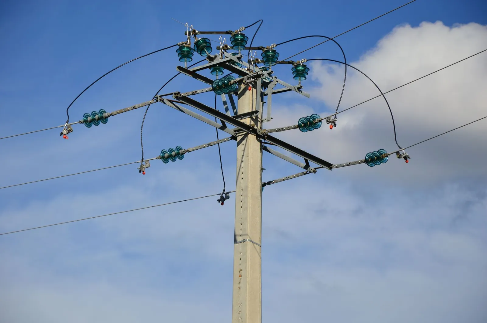 A high voltage power line stretching against a clear blue sky with clouds. Stock photo illustrating Quality Power Electrical Equipments' fund raise story.