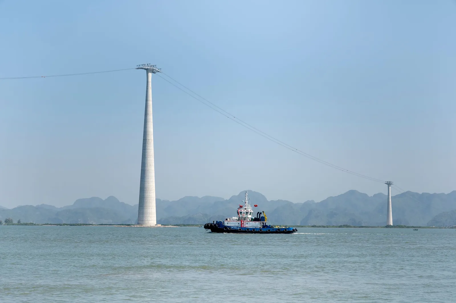 A tugboat navigates across a serene sea, passing under tall cable towers on a clear day. Stock photo illustrating Knowledge Marine & Engineering Works' new order story.