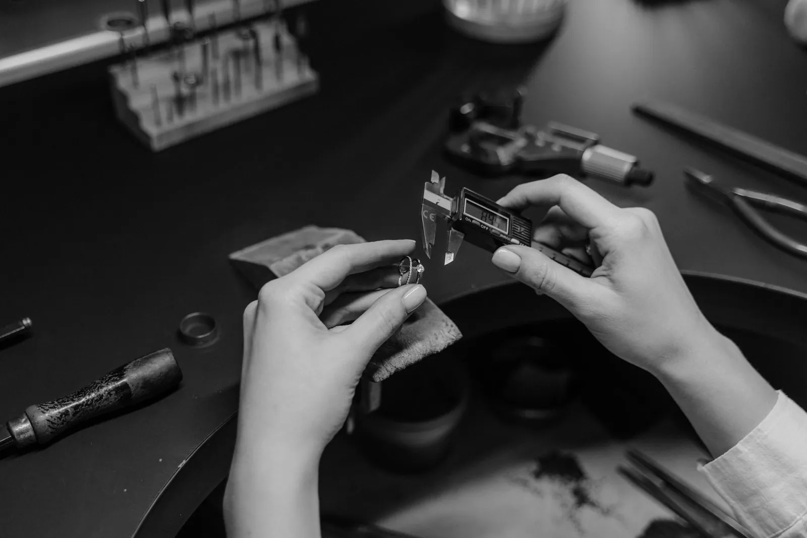 Black and white photo of a jeweler measuring a ring with a digital caliper in a workshop setting. Stock photo illustrating SJ Corporation's regulatory approval story.