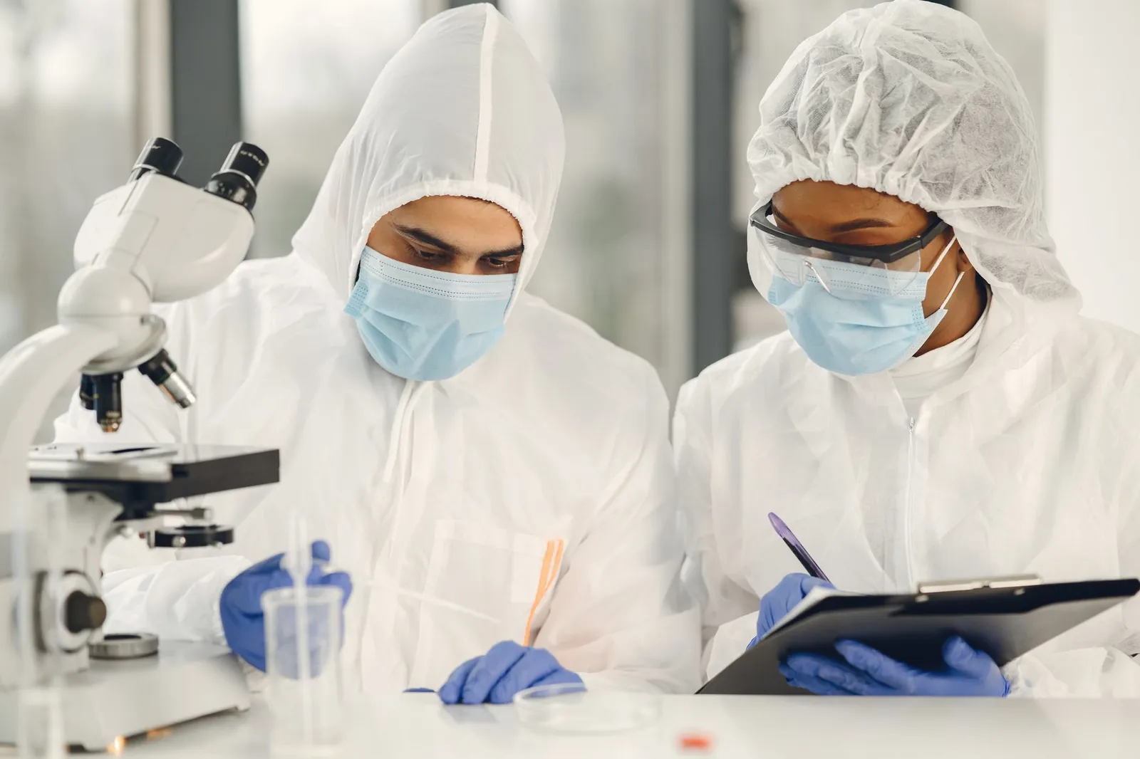 Two scientists in hazmat suits working with a microscope and notes in a laboratory setting. Stock photo illustrating Vijaypd Ceutical's partnership story.