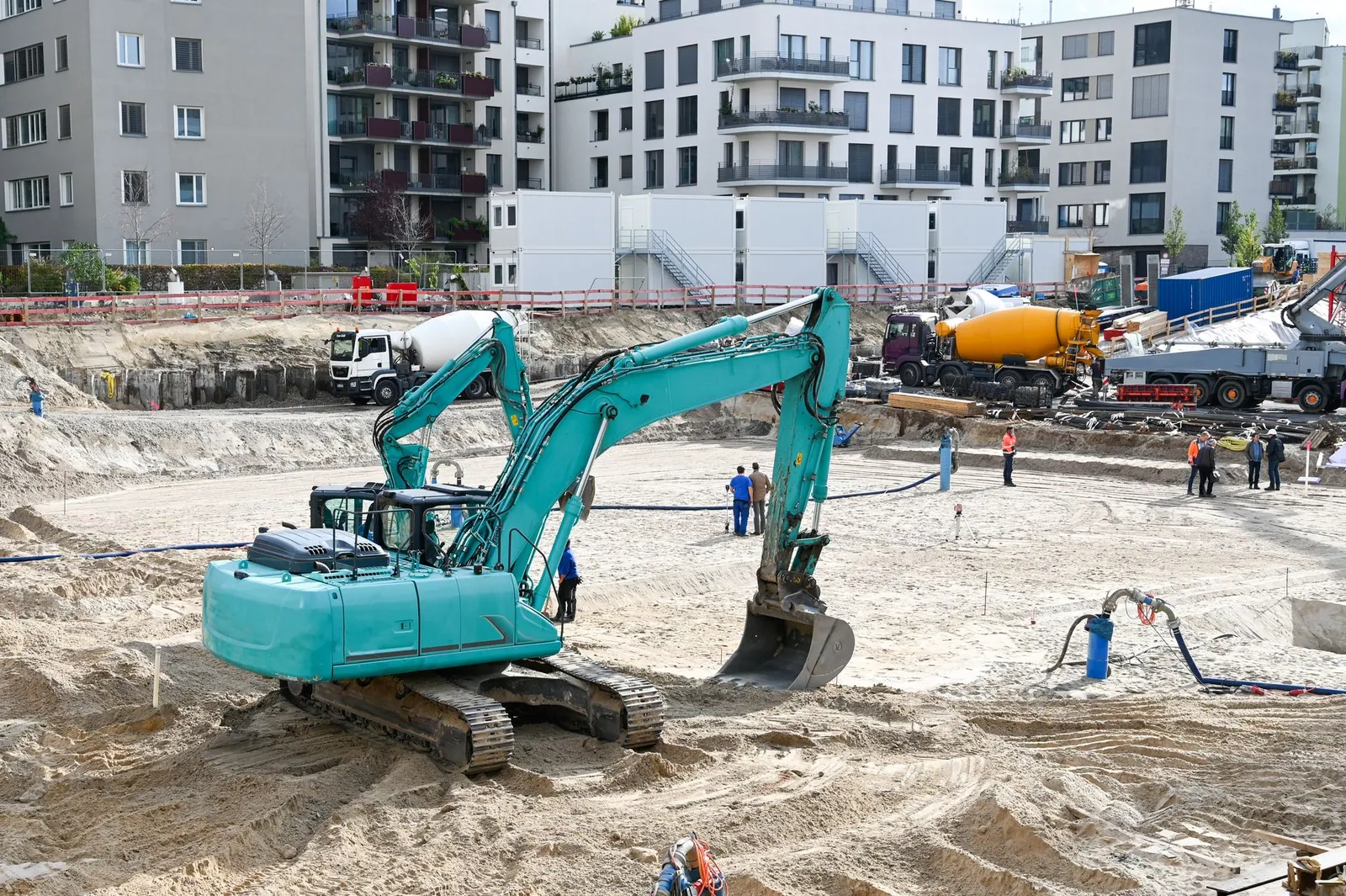 A busy construction site with machinery, workers, and residential buildings in the background. Stock photo illustrating Raymond Realty's fund raise story.