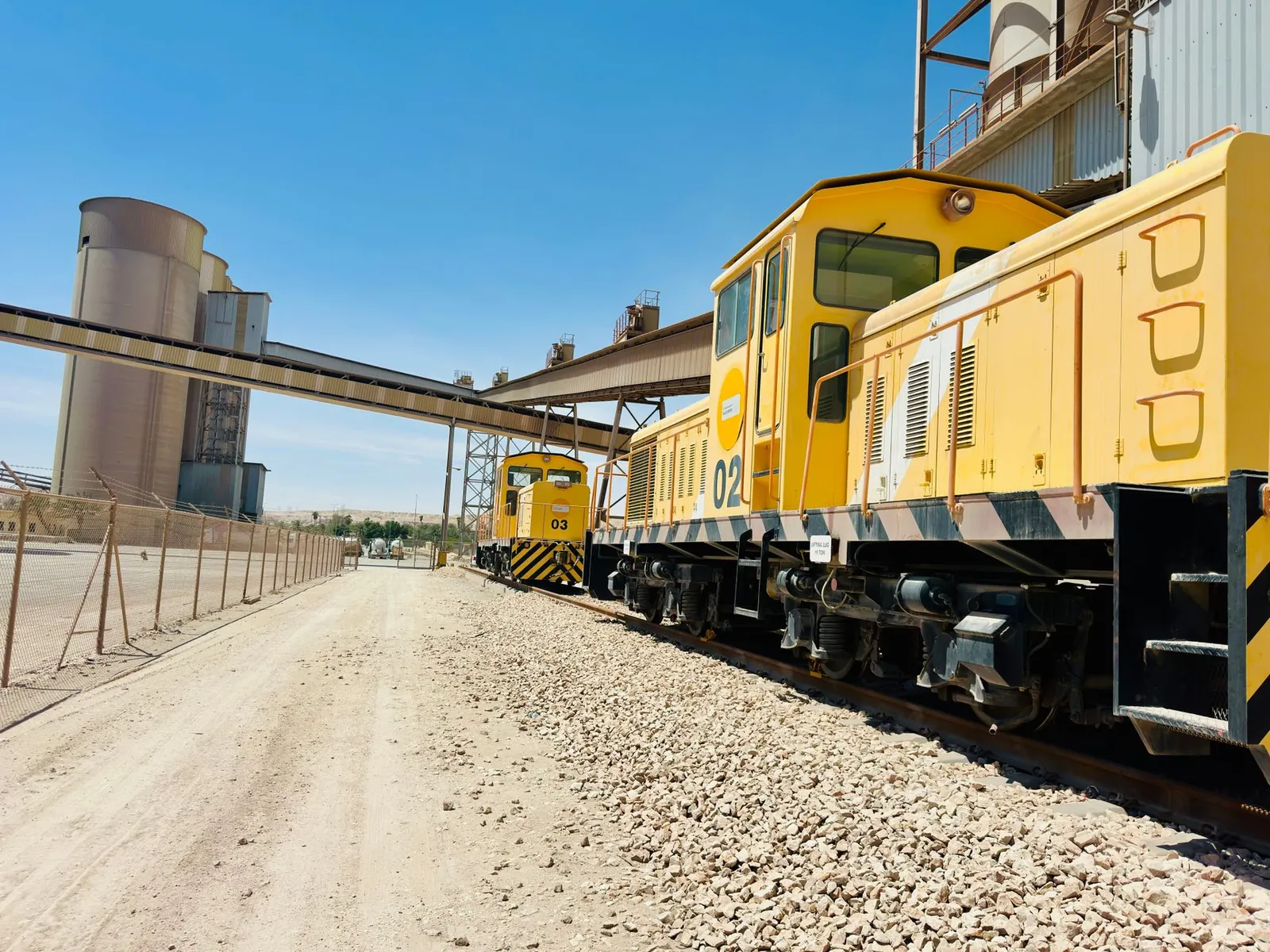 Yellow industrial trains on a railway track next to a cement plant on a clear day. Stock photo illustrating Sagar Cements' production started story.
