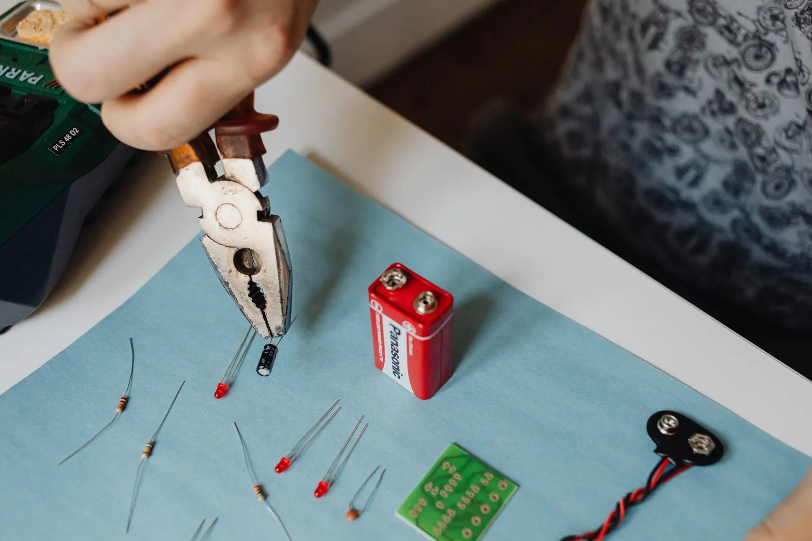 Close-up of electronics repair using pliers with resistors and battery. Stock photo illustrating DCX Systems' new order story.