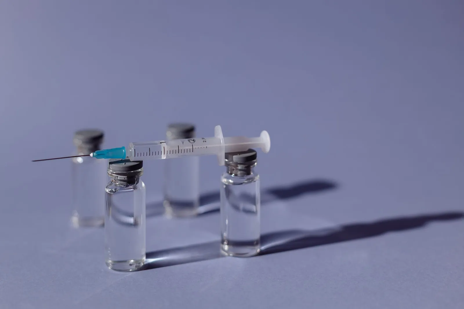 A syringe balanced on vaccine vials with a purple backdrop, representing medical treatment. Stock photo illustrating Glenmark Pharmaceuticals' product launched story.