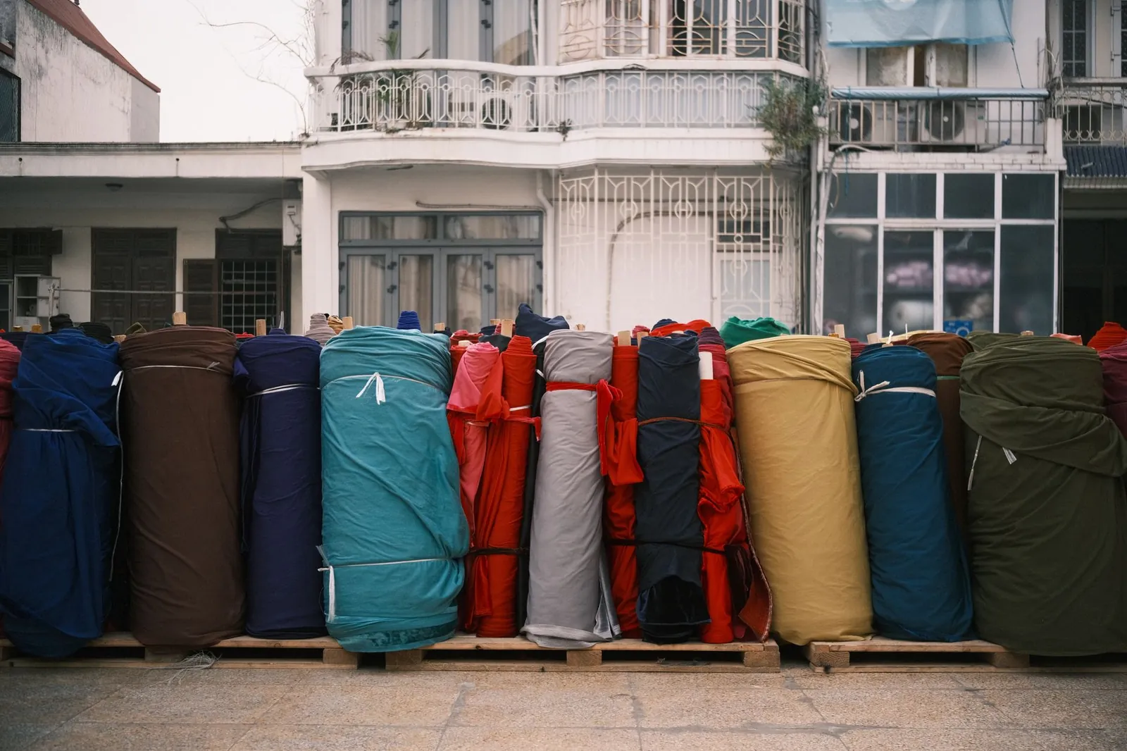 Vibrant rolls of fabric arranged outside an old building, creating a colorful display. Ideal for textile and design themes. Stock photo illustrating Candour Techtex's new order story.