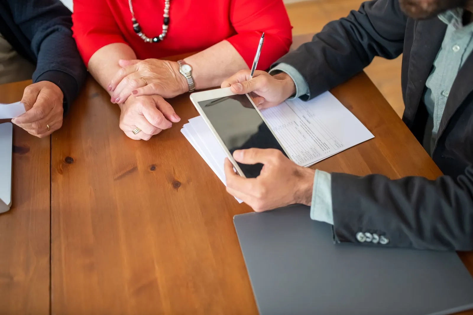 Business meeting at a wooden table with consultant reviewing documents and using a digital tablet. Stock photo illustrating PB Fintech's earning call story.