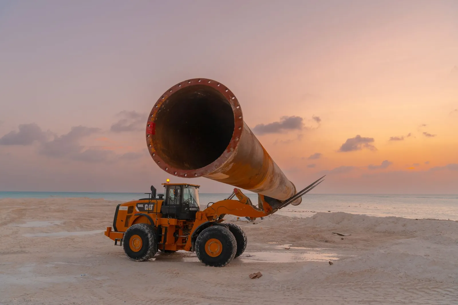 Construction equipment at sunset on a beach, featuring heavy machinery and large pipe work. Stock photo illustrating EMS's new order story.