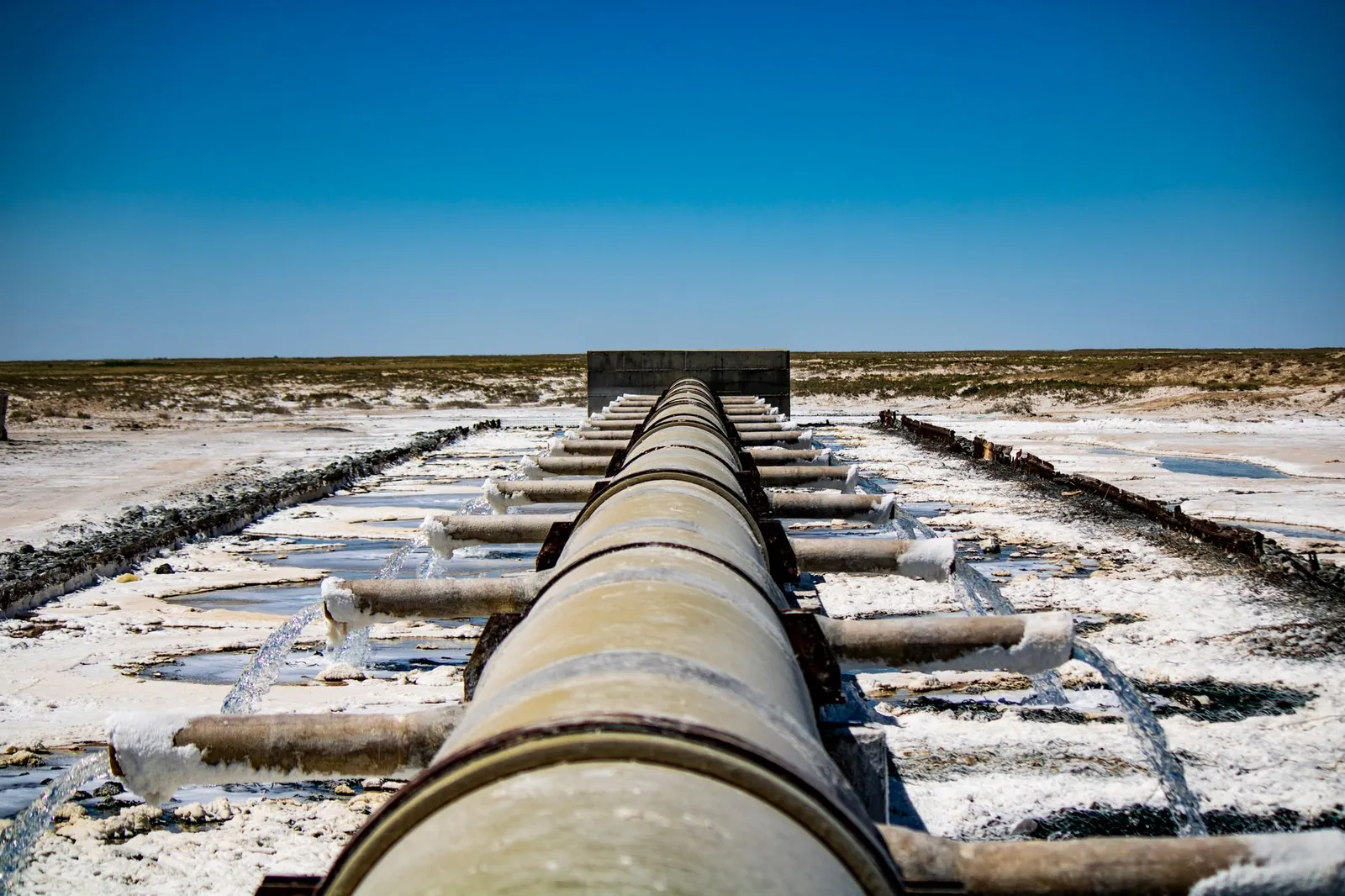 Large industrial pipeline discharging wastewater in arid, rural landscape under clear blue sky. Stock photo illustrating Concord Enviro Systems' new order story.