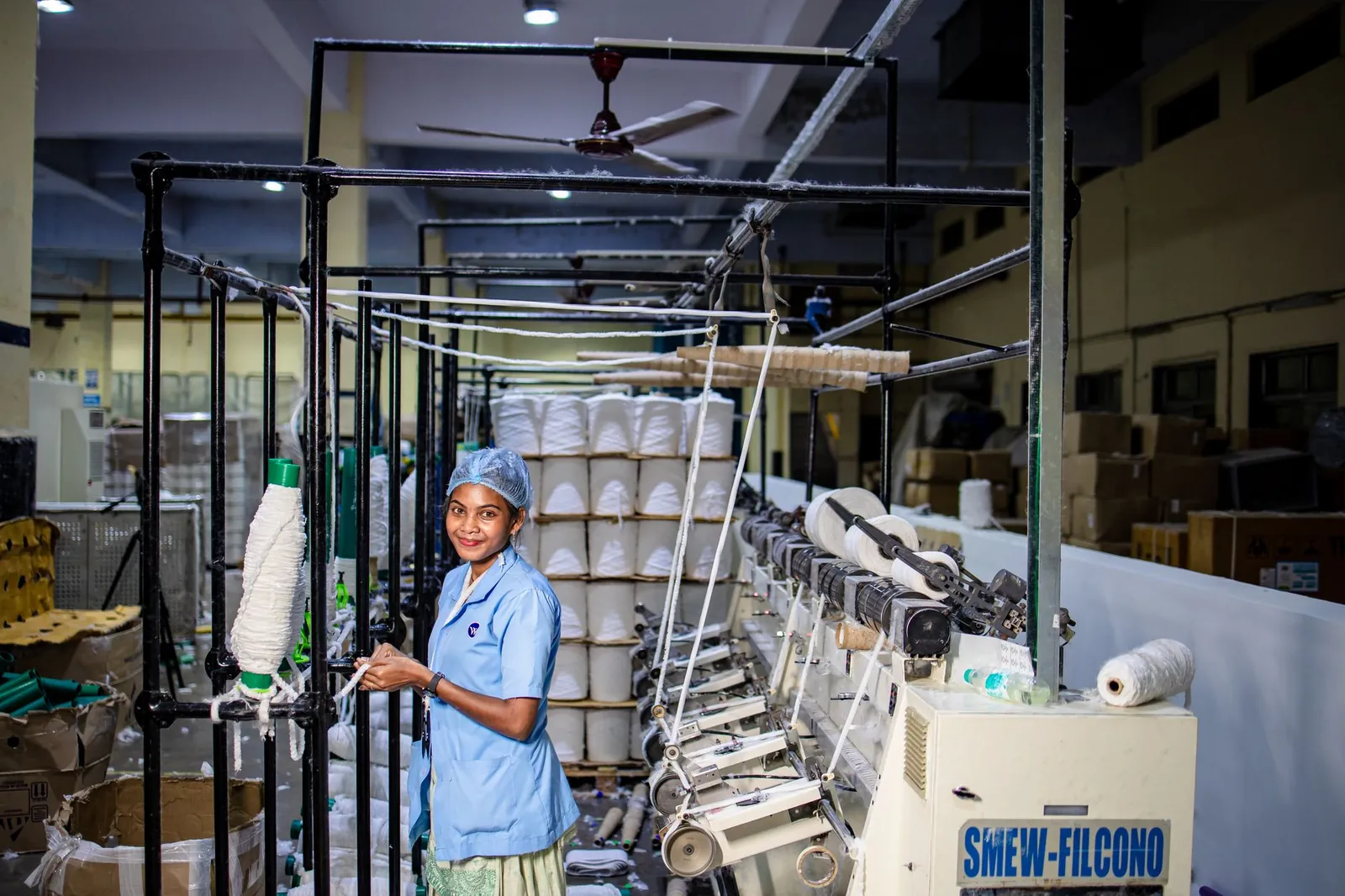 A female worker operates machinery in a textile spinning mill, smiling. Stock photo illustrating Rudra Ecovation's regulatory approval story.