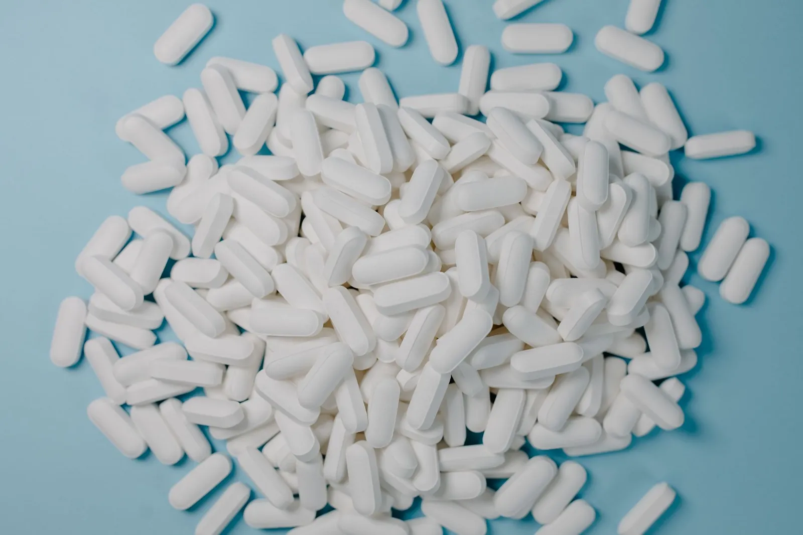 A collection of white oblong pills scattered on a blue surface, healthcare and medication concept. Stock photo illustrating Lupin's earning call story.