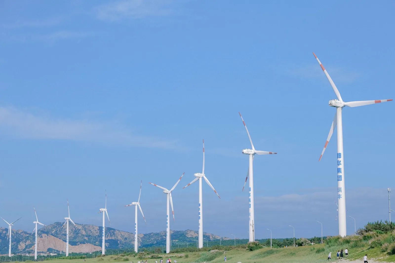 Row of wind turbines against blue sky in Weihai, promoting renewable energy. Stock photo illustrating Advait Energy Transitions' earning call story.