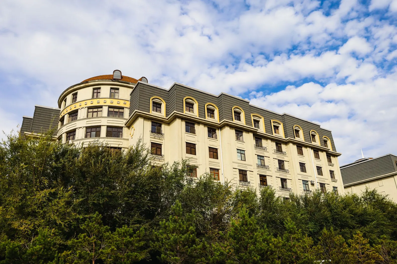 A stylish multi-storey hotel exterior with lush greenery and a vibrant cloudy sky backdrop. Stock photo illustrating Yatharth Hospital & Trauma Care Services' fund raise story.