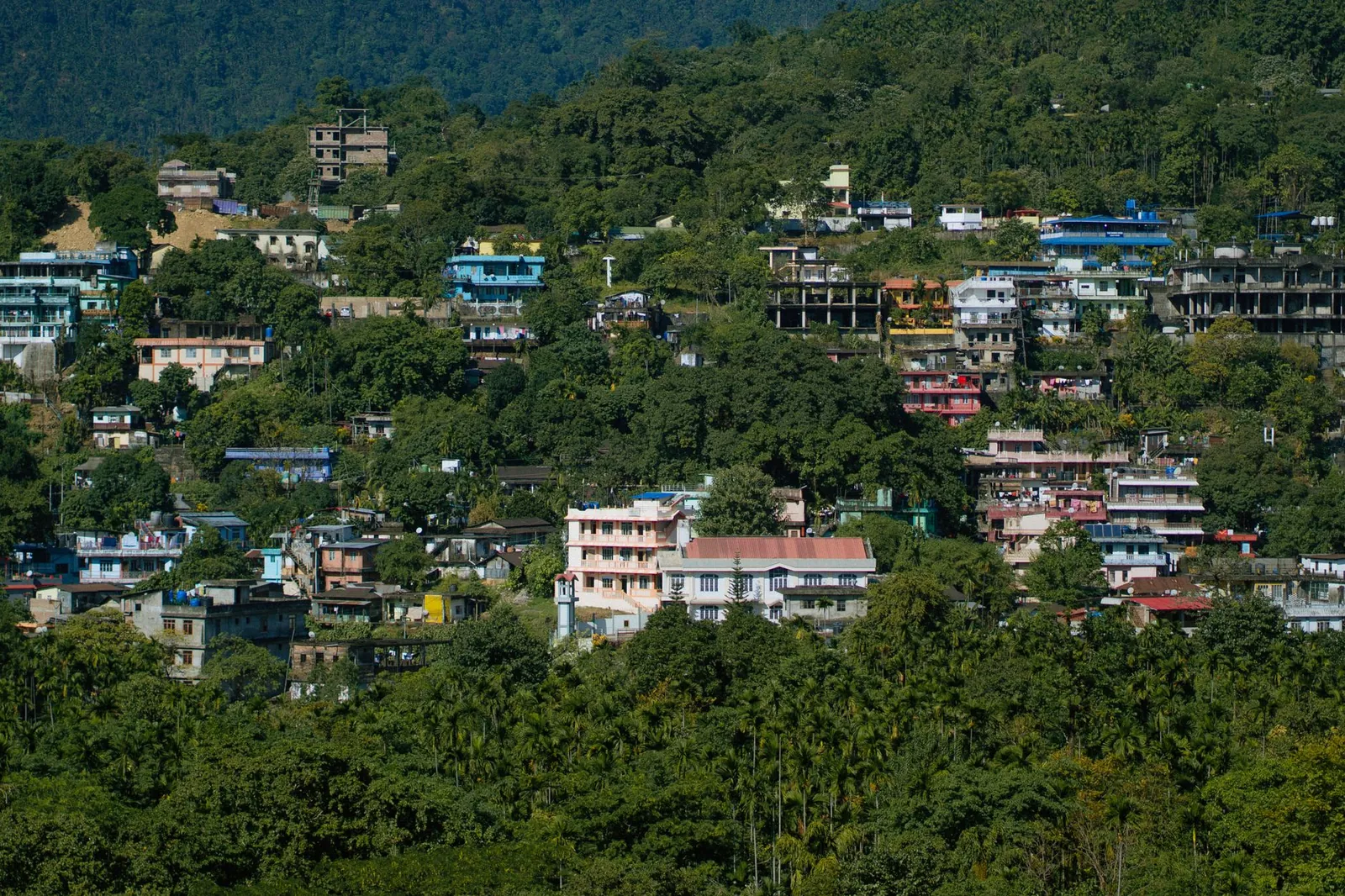 A vibrant hillside town with colorful buildings surrounded by lush greenery, showcasing a serene rural landscape. Stock photo illustrating Lemon Tree Hotels' partnership story.