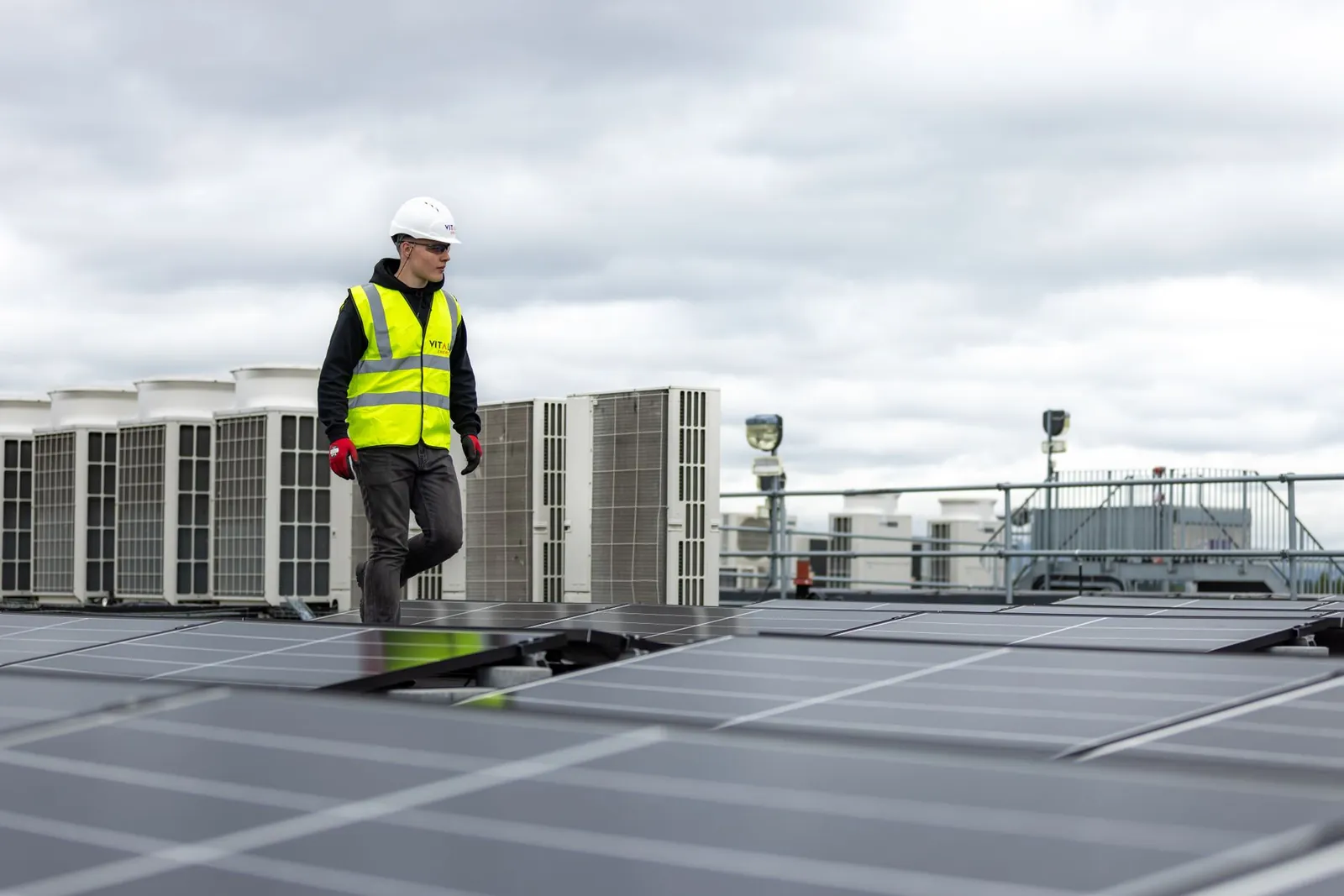 Engineer in safety gear inspecting solar panels on a rooftop under a cloudy sky. Stock photo illustrating Vikran Engineering's new order story.