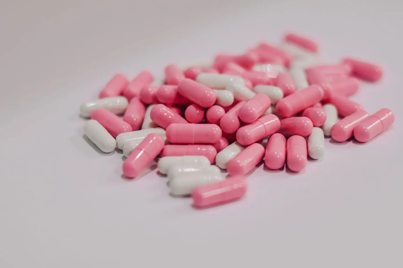 Close-up of pink and white pharmaceutical capsules scattered on a white surface. Stock photo illustrating Granules India's promoter buying story.