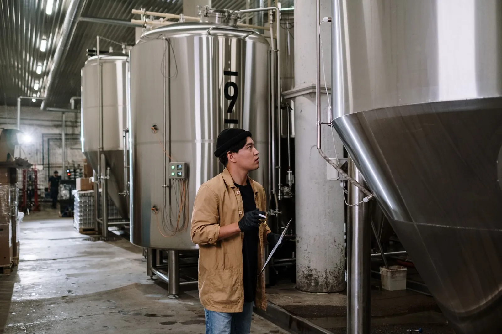 Asian man inspecting stainless steel tanks in a brewery, showcasing modern industrial processes. Stock photo illustrating Jindal Stainless' partnership story.