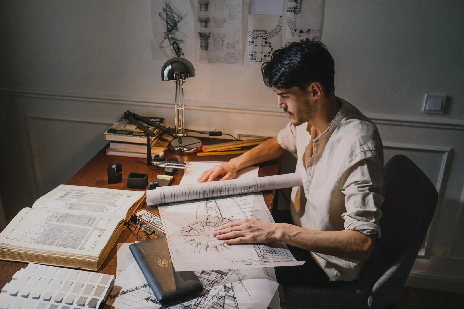 Young architect at a desk working on blueprint designs under lamp light. Stock photo illustrating Garden Reach Shipbuilders & Engineers' expansion story.