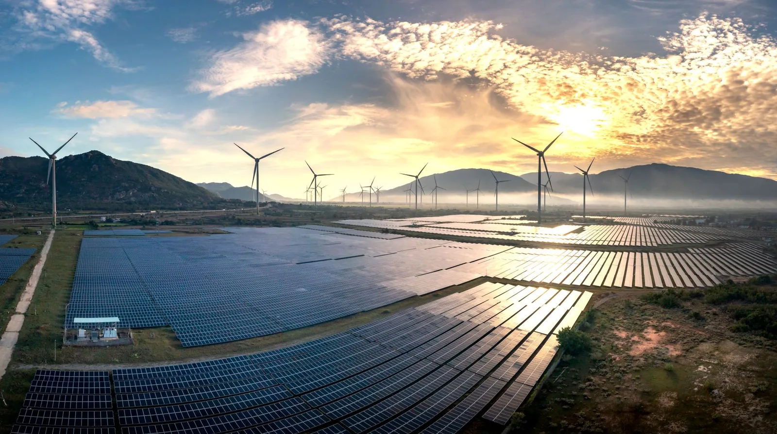 Aerial photograph capturing solar panels and wind turbines under a stunning sunrise. Sustainable energy landscape. Stock photo illustrating Suzlon Energy's earning call story.