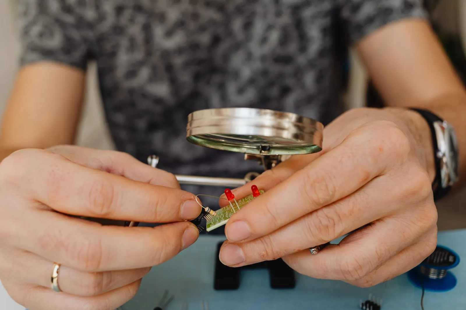 Close-up view of a person fixing an electronic circuit board with a magnifier. Stock photo illustrating Syrma SGS Technology's financial results story.