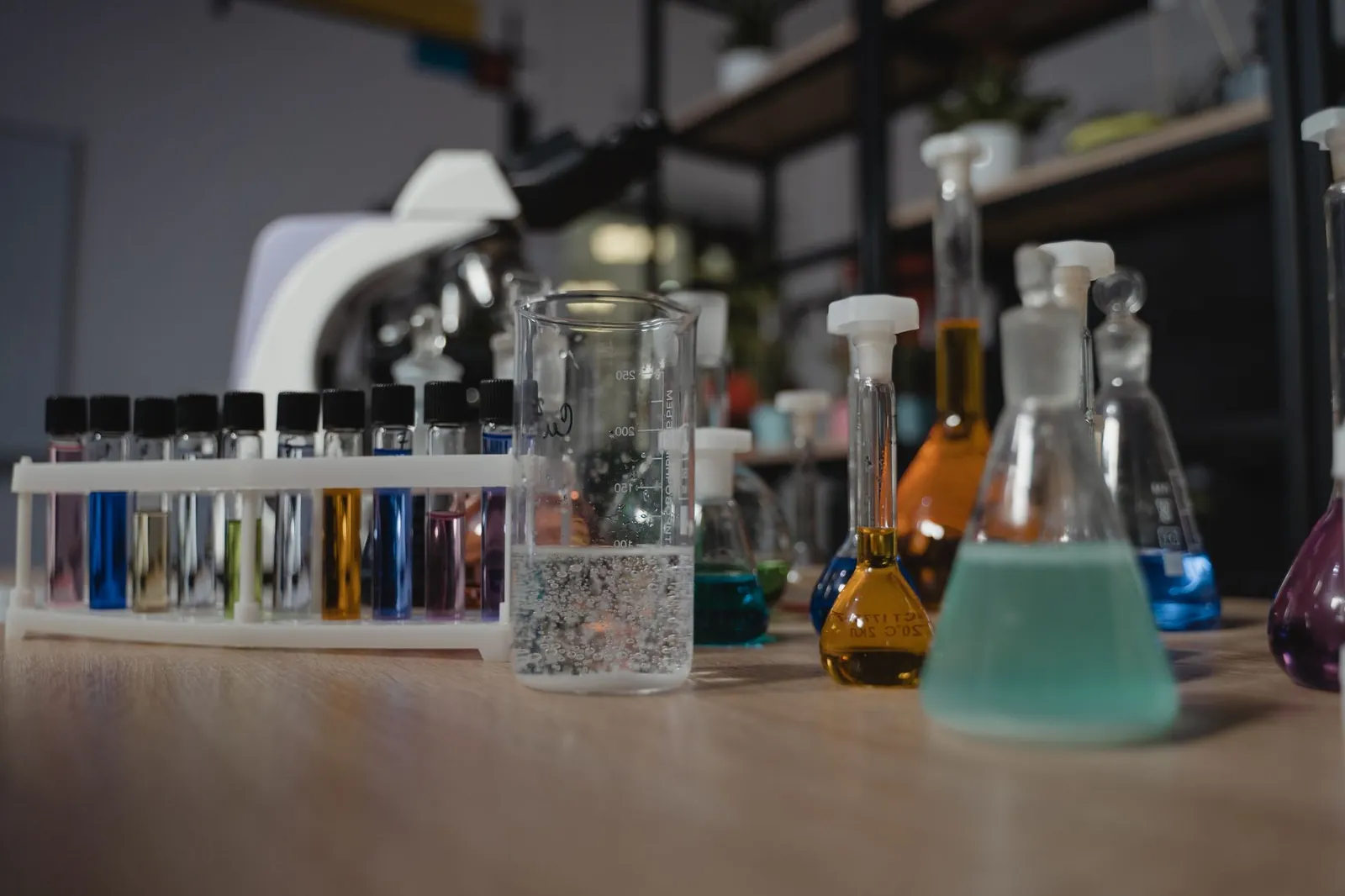 Glassware with colored liquids in a laboratory on a wooden table, showcasing diverse chemical research tools. Stock photo illustrating Acutaas Chemicals' regulatory approval story.