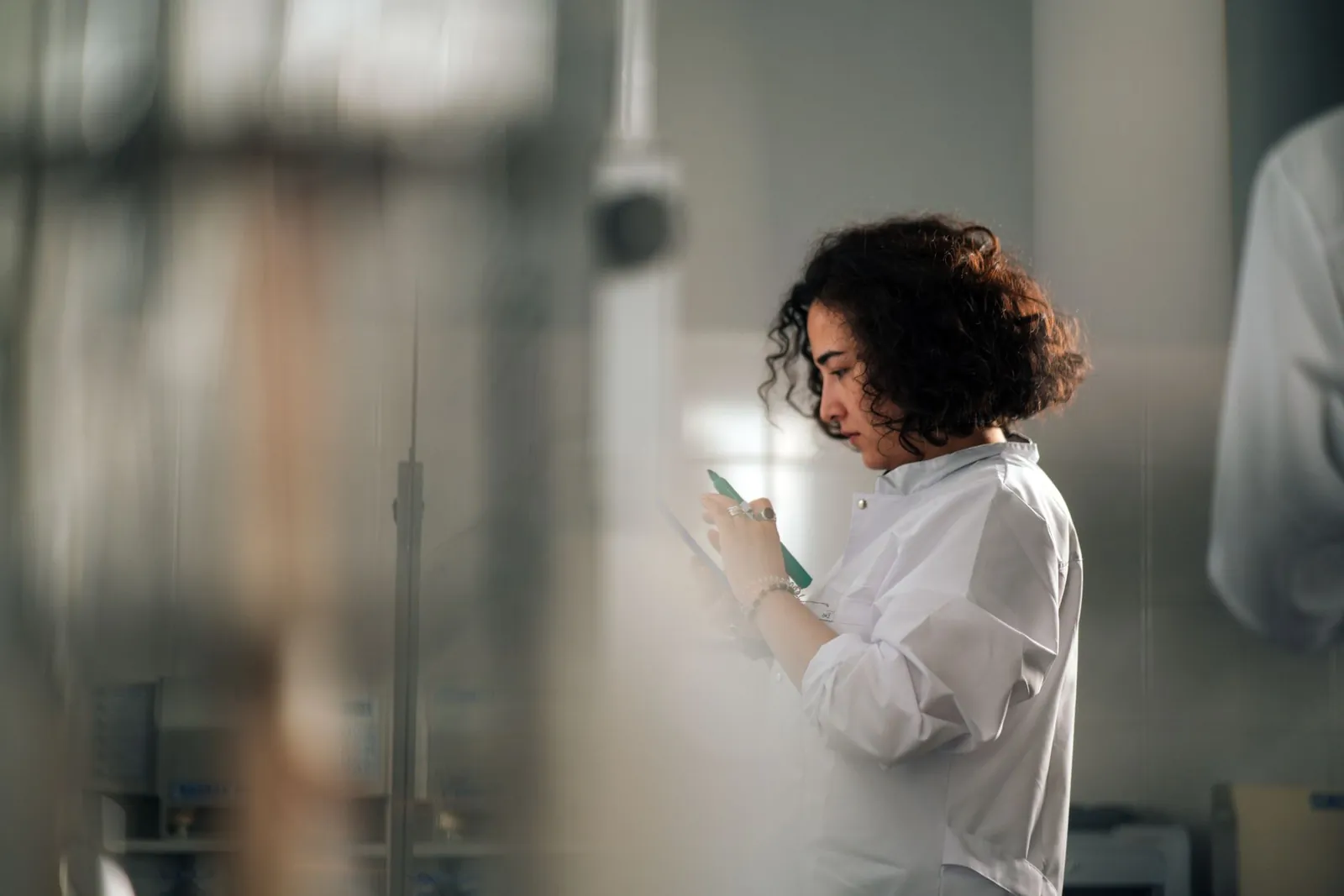 A focused female scientist with curly hair writes notes in a laboratory setting. Stock photo illustrating Bajaj Healthcare's earning call story.