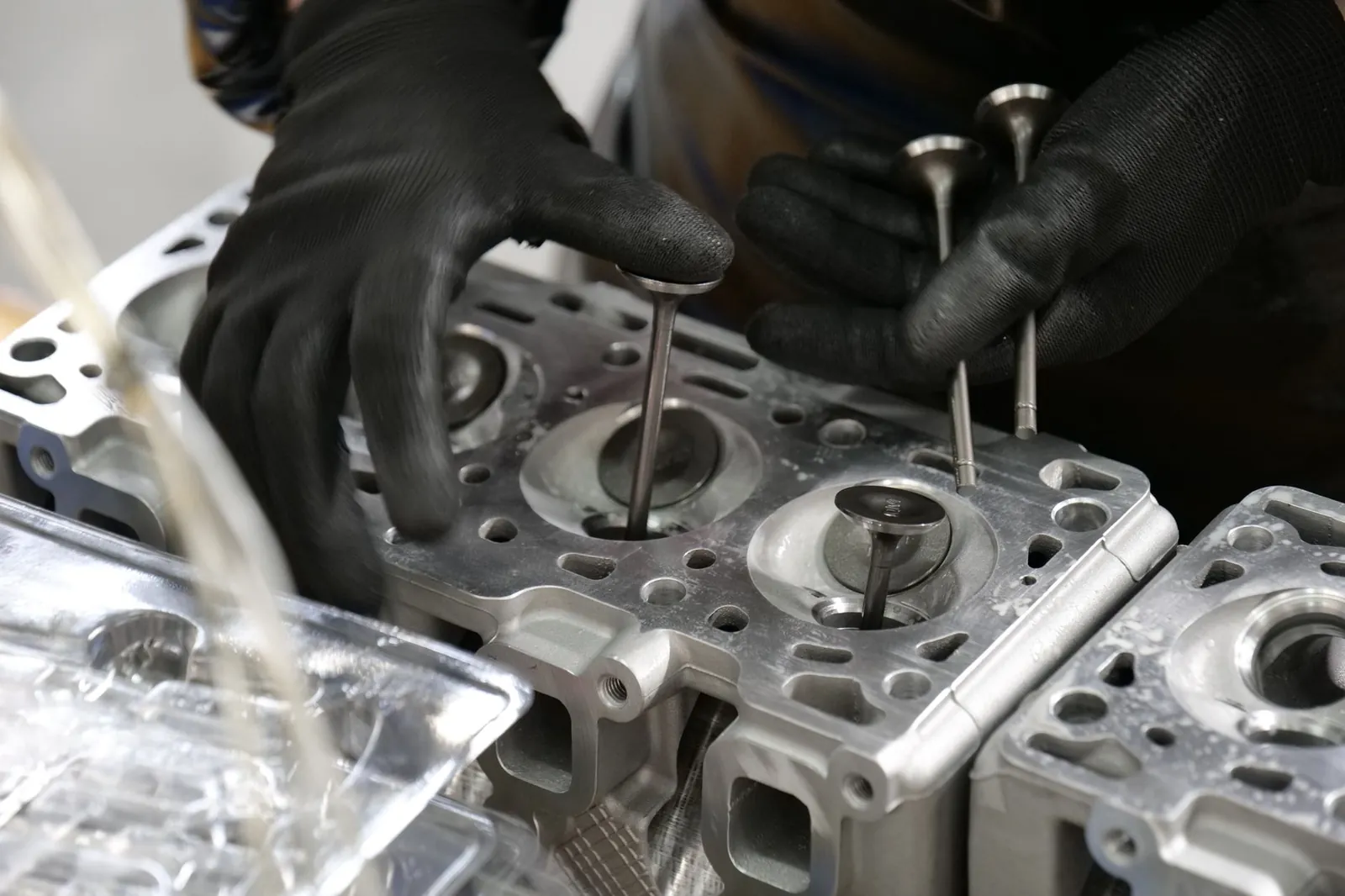Close-up of mechanic's hands working on engine cylinder head assembly with valves. Stock photo illustrating Samvardhana Motherson International's fund raise story.