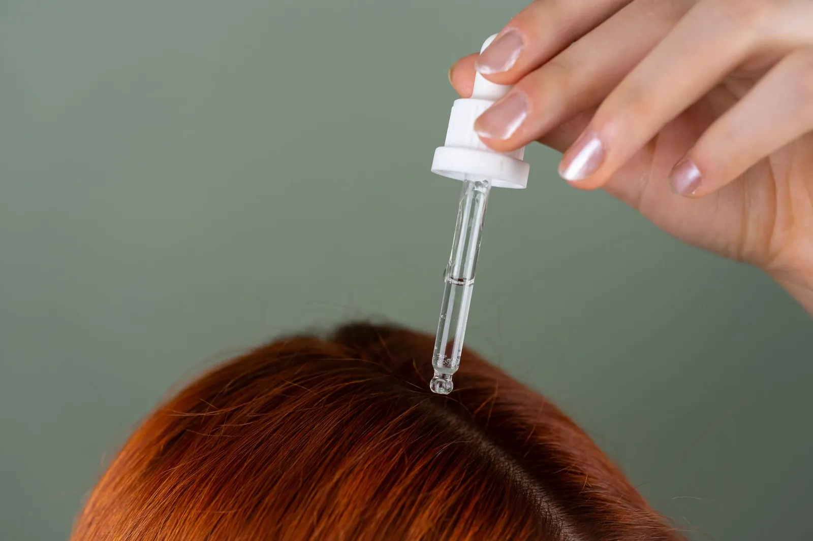 Close-up of applying serum to roots with a precision dropper on red hair, showcasing hair care routine. Stock photo illustrating Alkem Laboratories' product launched story.