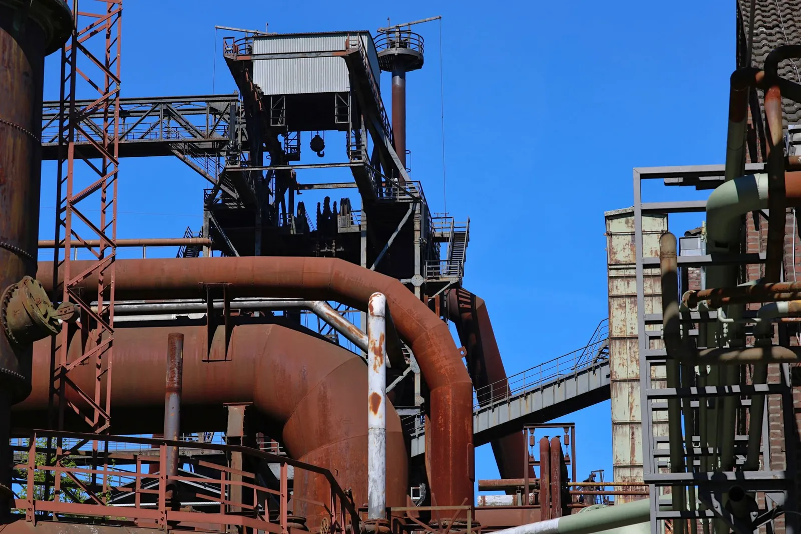 Detailed view of an industrial complex featuring rusted steel pipes and structures under a clear blue sky. Stock photo illustrating Shah Alloys' promoter buying story.