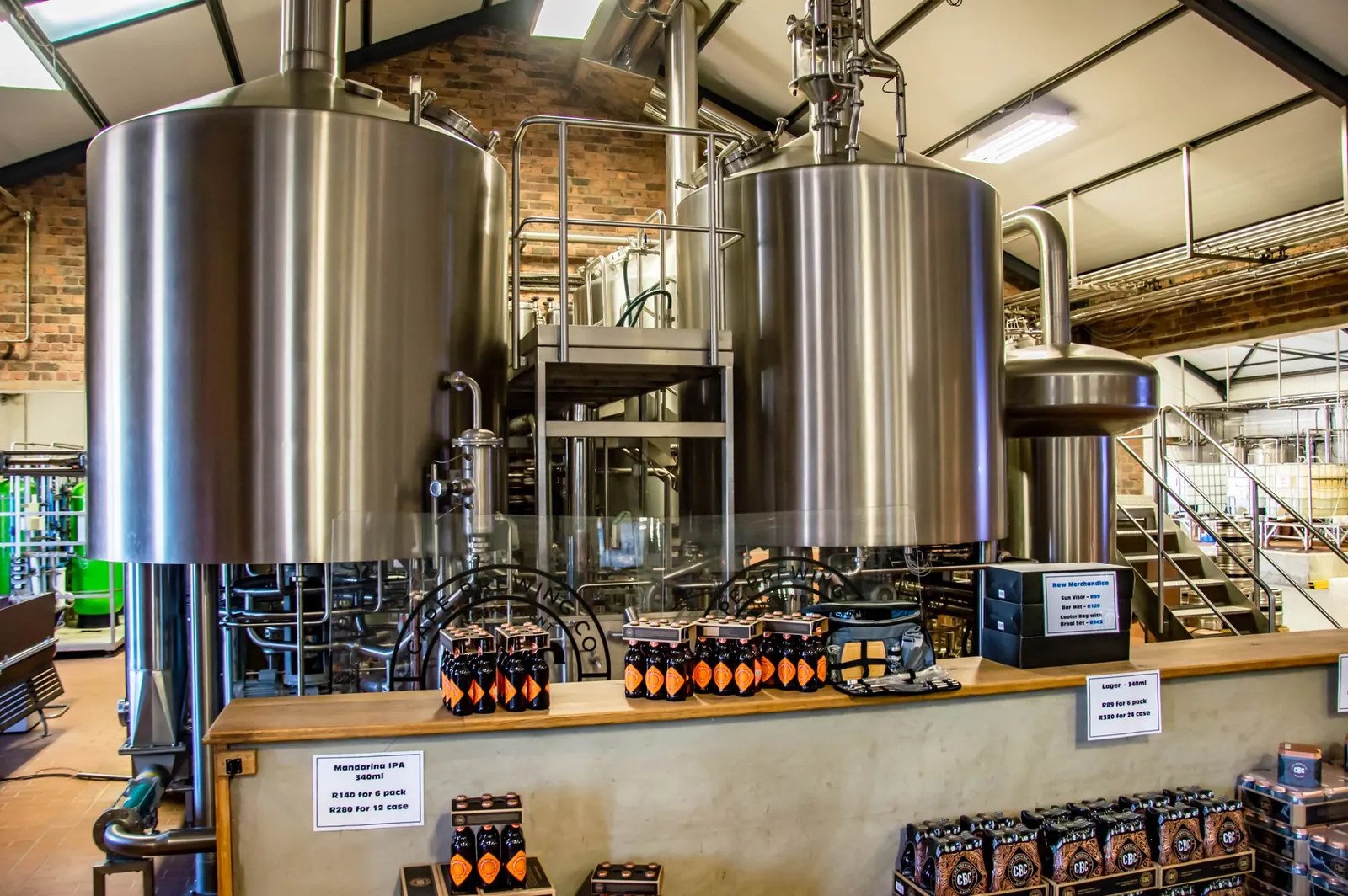 Interior of a brewery showcasing large stainless steel tanks and bottled beverages on display. Stock photo illustrating Som Distilleries & Breweries' production started story.