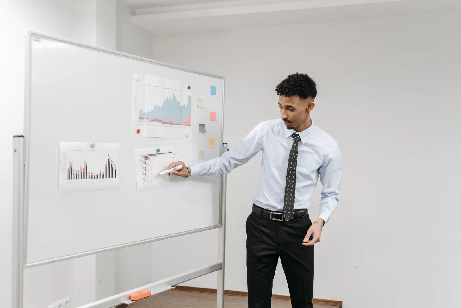 Man presenting charts on a whiteboard during a business meeting in a contemporary office. Stock photo for the ALFA News guide: Understanding Standalone vs Consolidated Results for Indian Stocks.