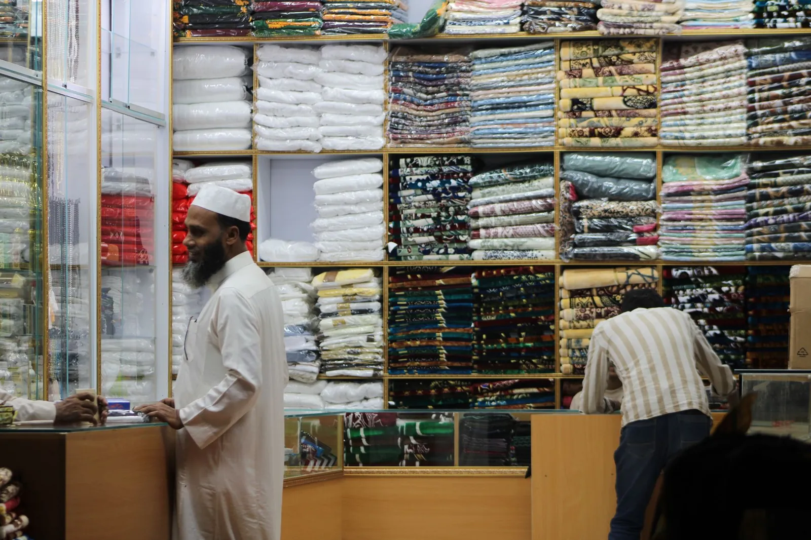 Two men interacting in a colorful fabric store filled with various textiles and cloth materials. Stock photo illustrating V2 Retail's earning call story.