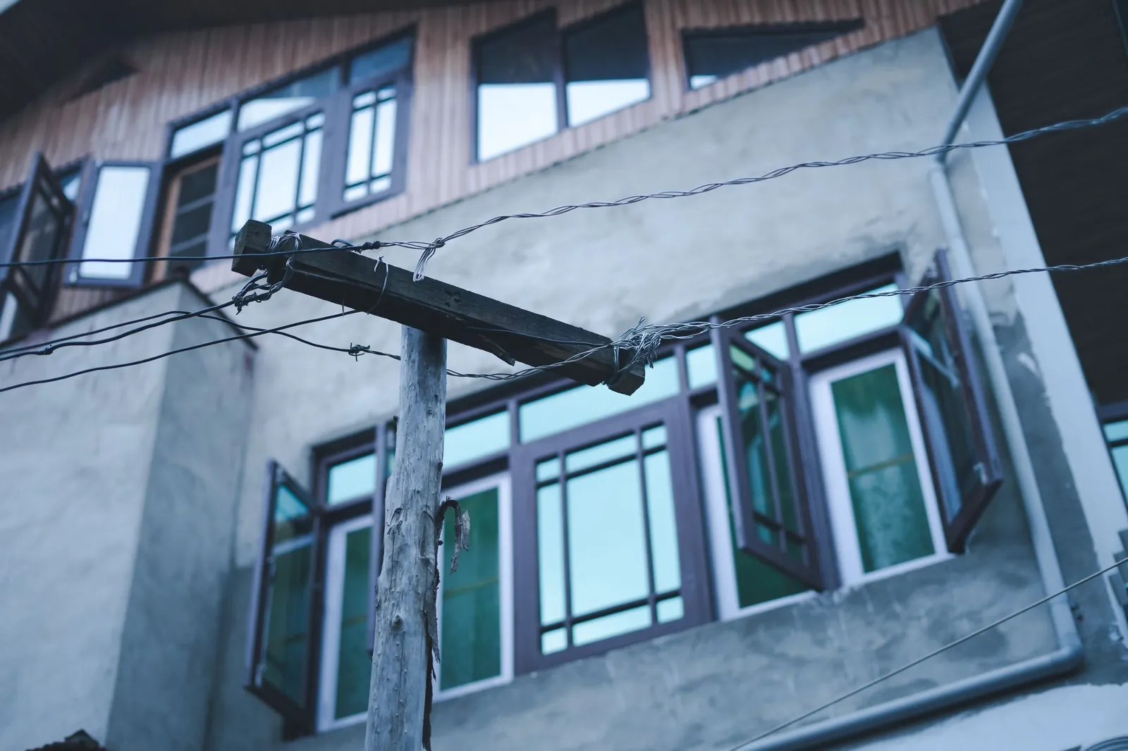 Wooden power pole with electricity wires against an urban building with open windows in Srinagar. Stock photo illustrating Sugs Lloyd's new order story.
