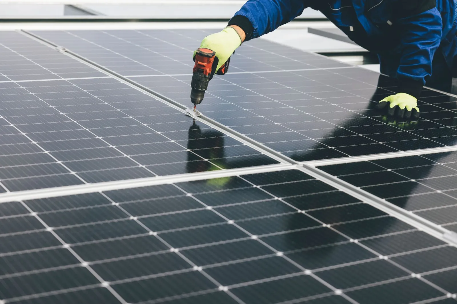 A technician uses a power tool to install solar panels, showcasing renewable energy efforts. Stock photo illustrating GK Energy's earning call story.