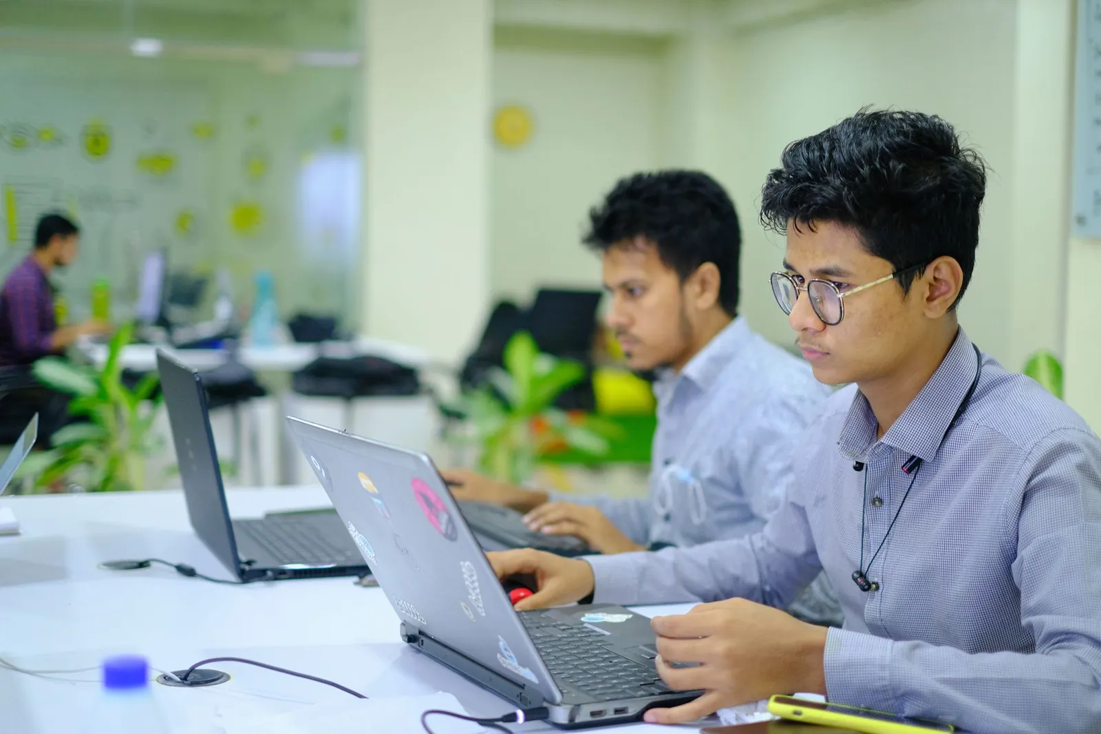 Two young professionals working on laptops in a vibrant and modern office setting. Stock photo illustrating Ace Alpha Tech's financial results story.