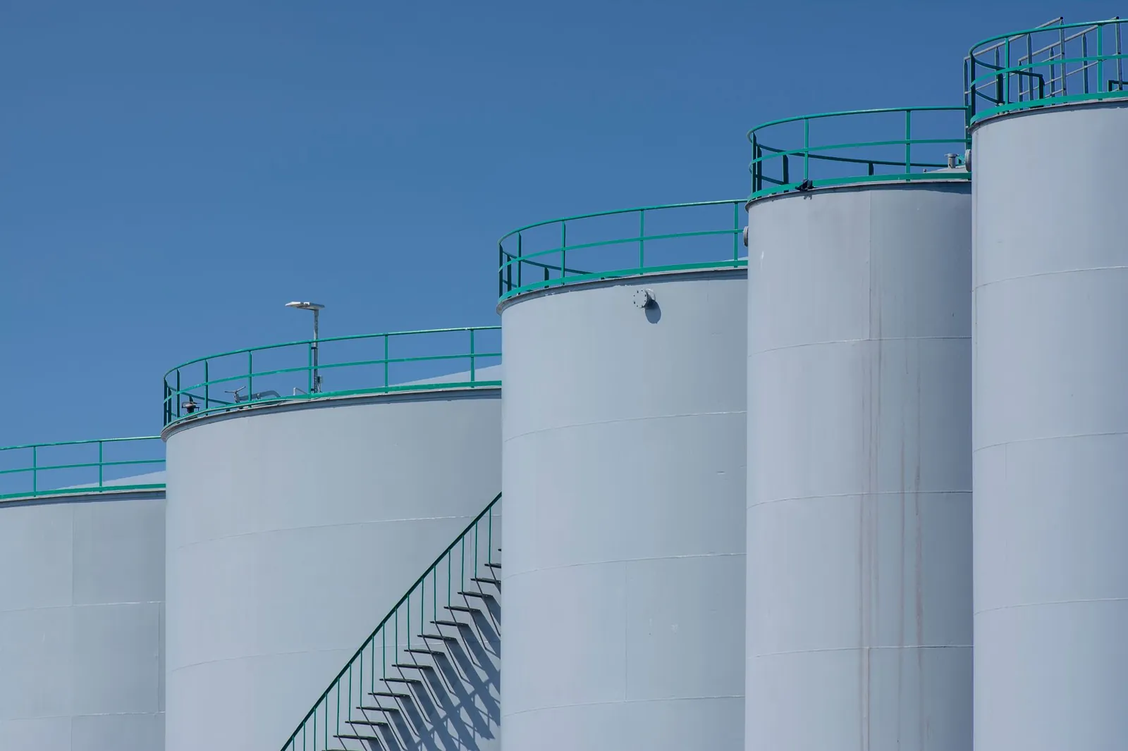 Large industrial storage tanks with green railings against a clear blue sky. Stock photo illustrating Ellenbarrie Industrial Gases' new order story.
