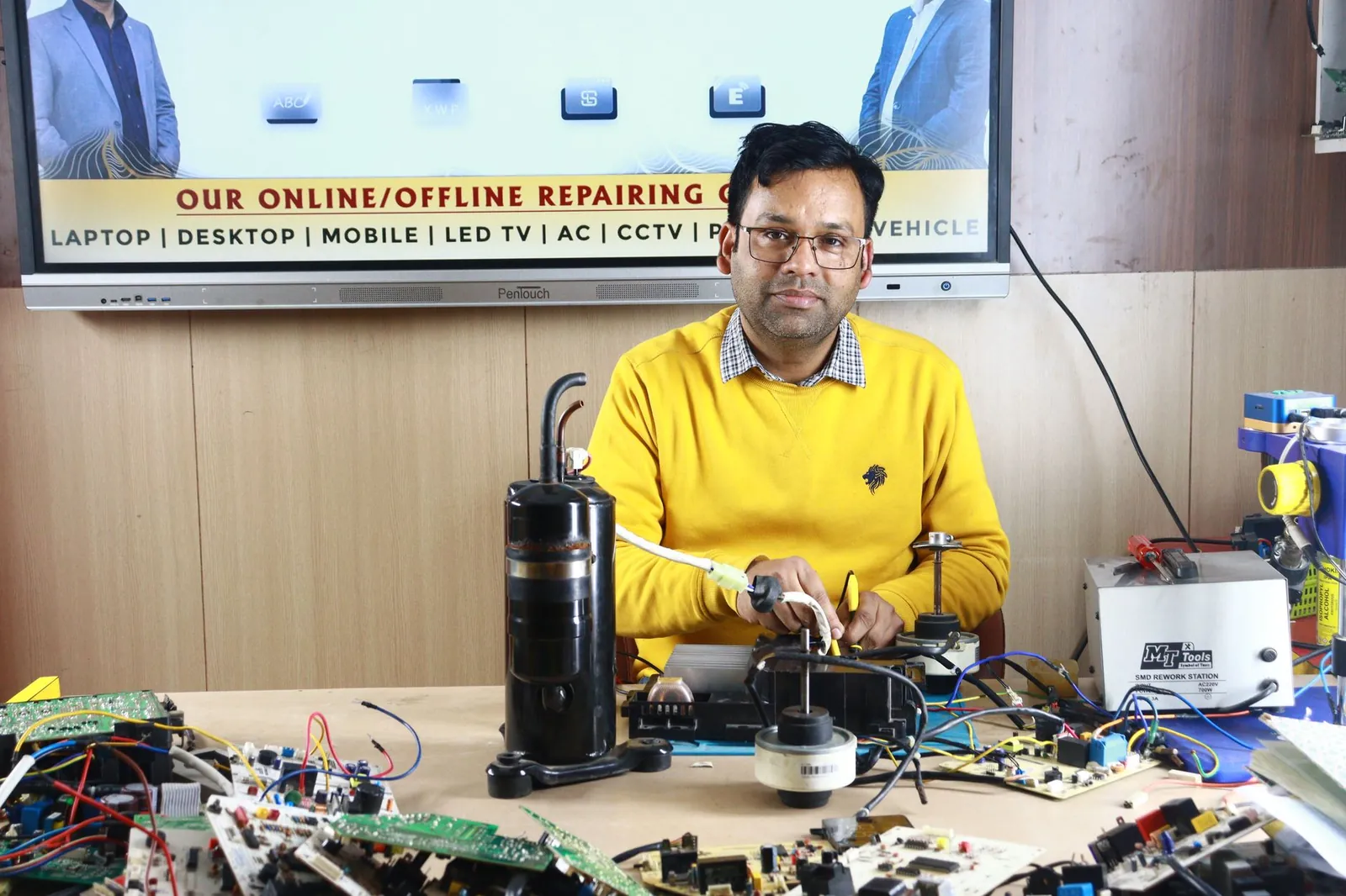 Man engages in air conditioner repair at New Delhi training center, surrounded by electronic components. Stock photo illustrating Compucom Software's new order story.