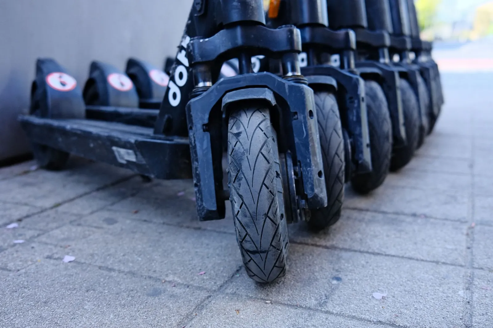 Row of parked electric scooters on a city sidewalk, focusing on wheels. Stock photo illustrating Ola Electric Mobility's fund raise story.