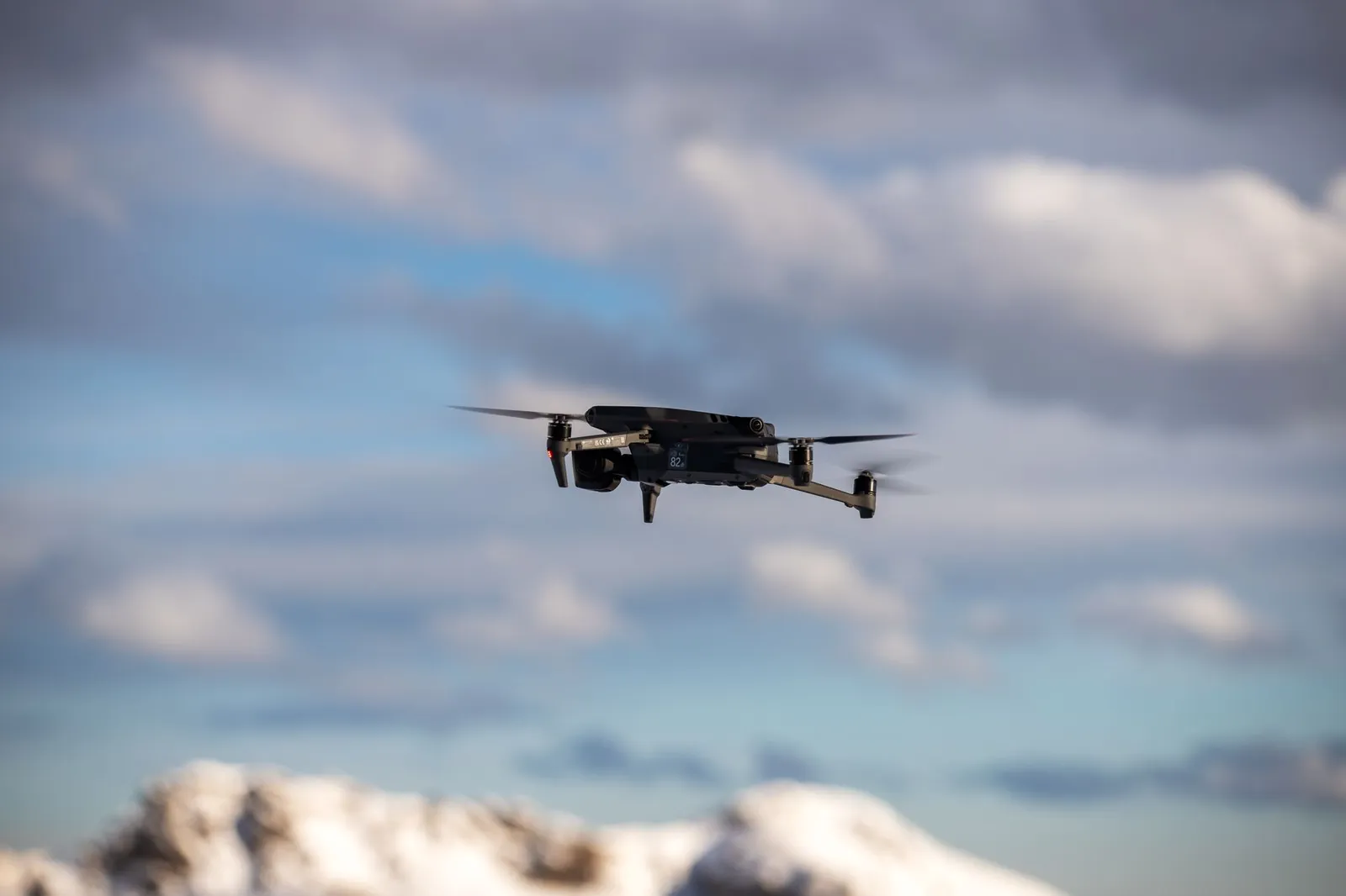 Aerial view of a drone flying over snow-covered mountains with dramatic clouds. Stock photo illustrating Zen Technologies' product launched story.