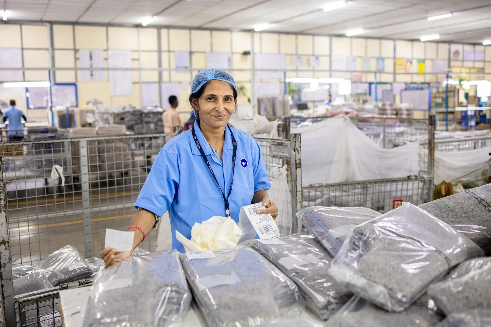 A female worker in blue uniform at a textile factory sorting packaged products. Stock photo illustrating Encompass Design India's fund raise story.
