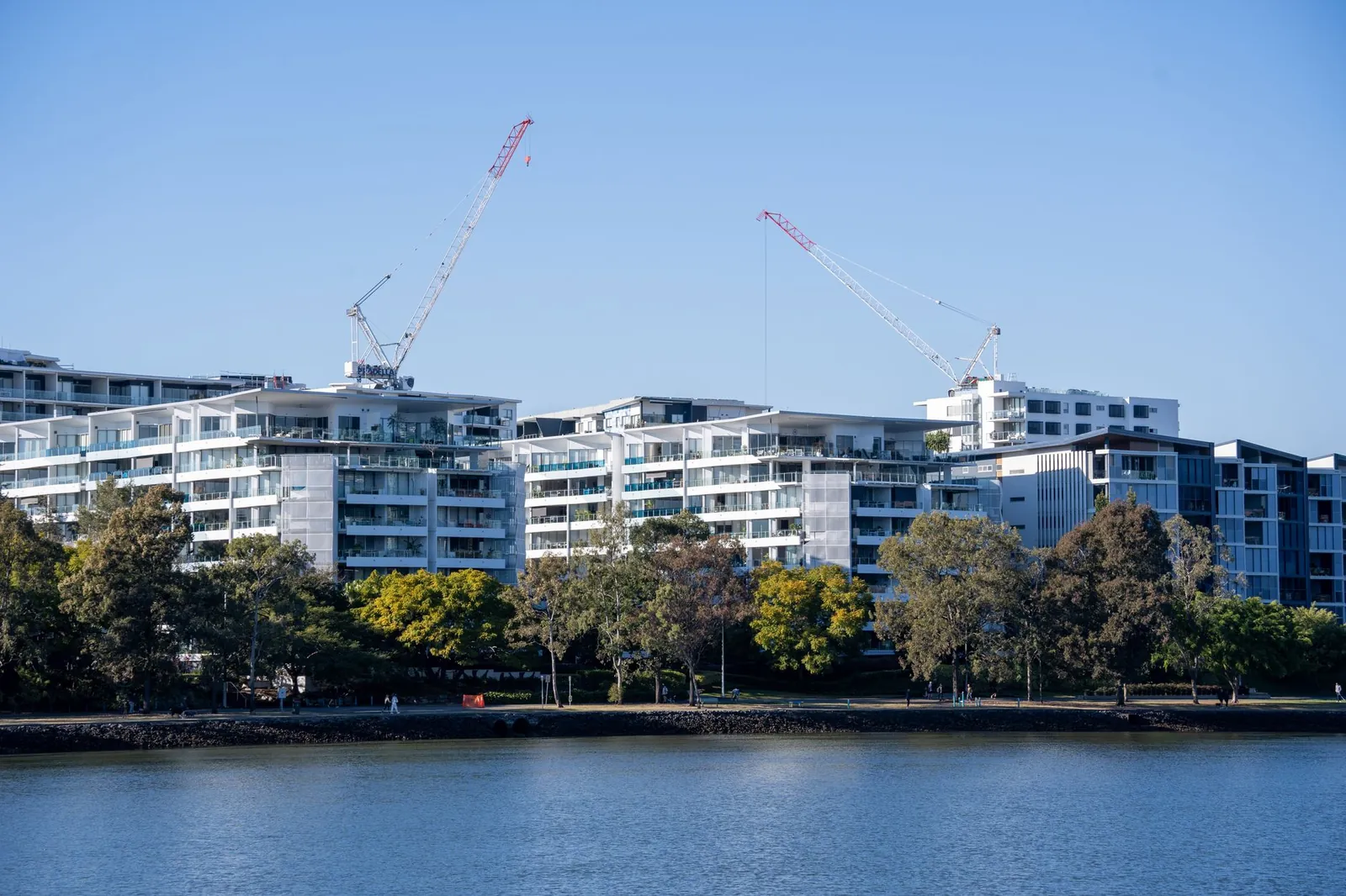 Luxurious riverside apartments under construction with cranes against a clear blue sky. Stock photo illustrating Brigade Hotel Ventures' expansion story.