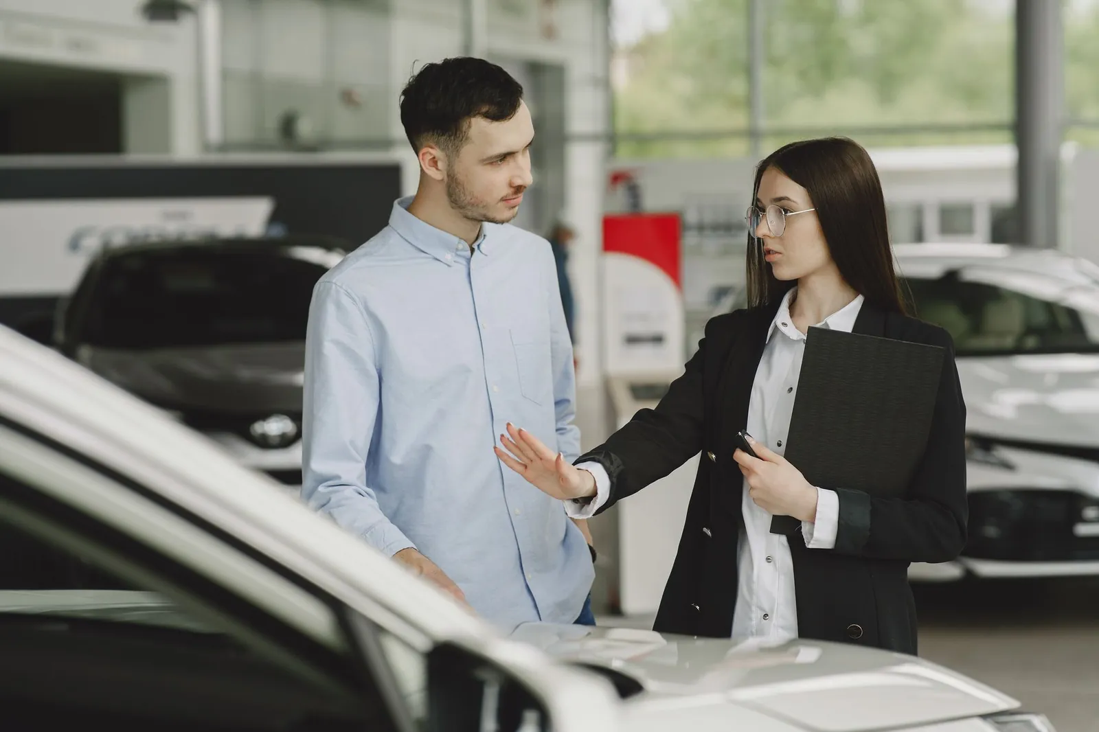 A salesperson and customer discussing car features in a dealership setting. Stock photo illustrating CarTrade Tech's product launched story.