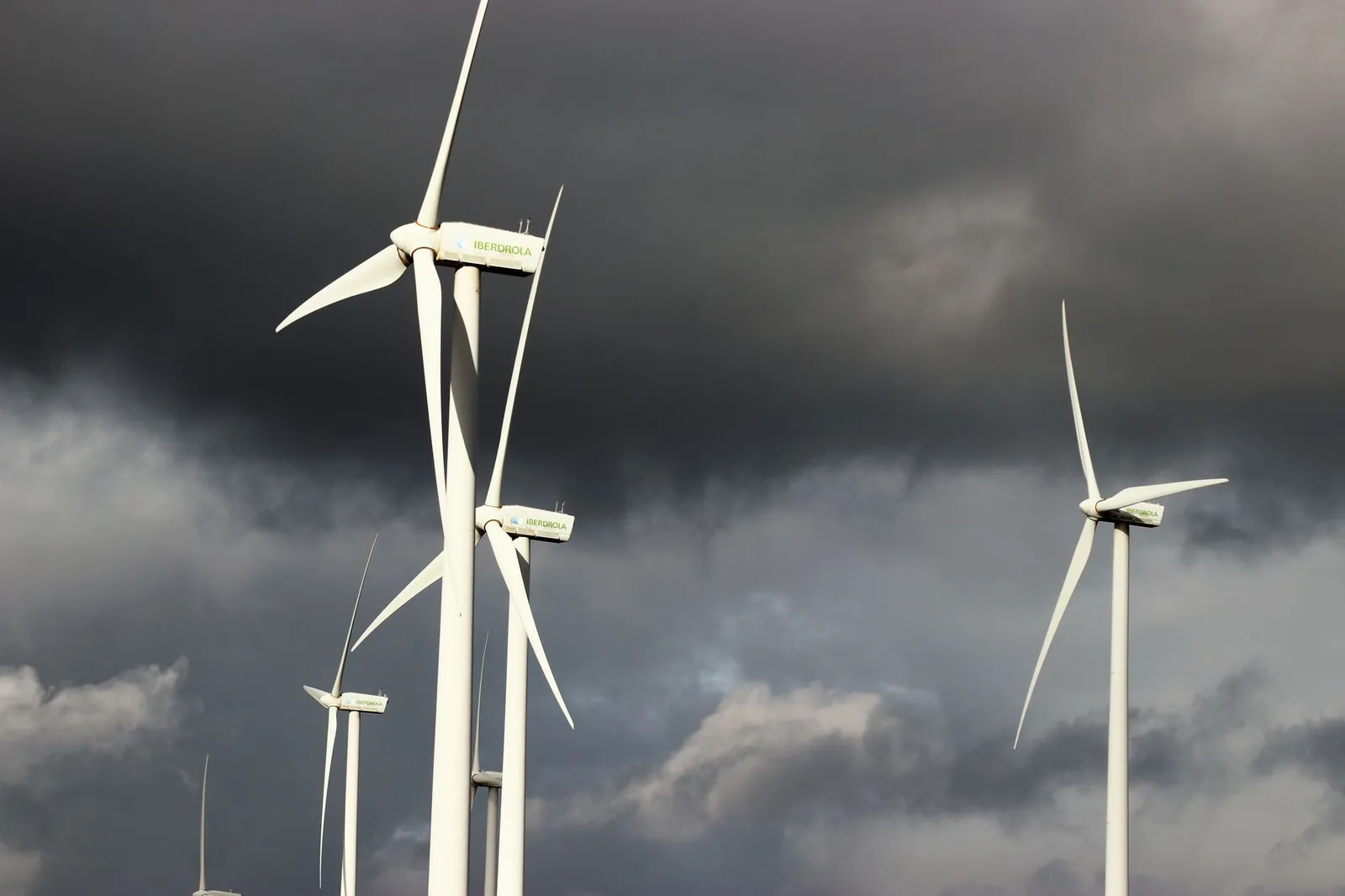 Wind turbines with dark storm clouds in the background, highlighting renewable energy amid powerful weather conditions. Stock photo illustrating ACME Solar Holdings' production started story.