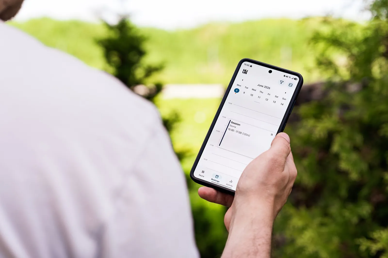 A person using a sauna booking app on a smartphone outdoors, surrounded by greenery. Stock photo illustrating RateGain Travel Technologies' product launched story.